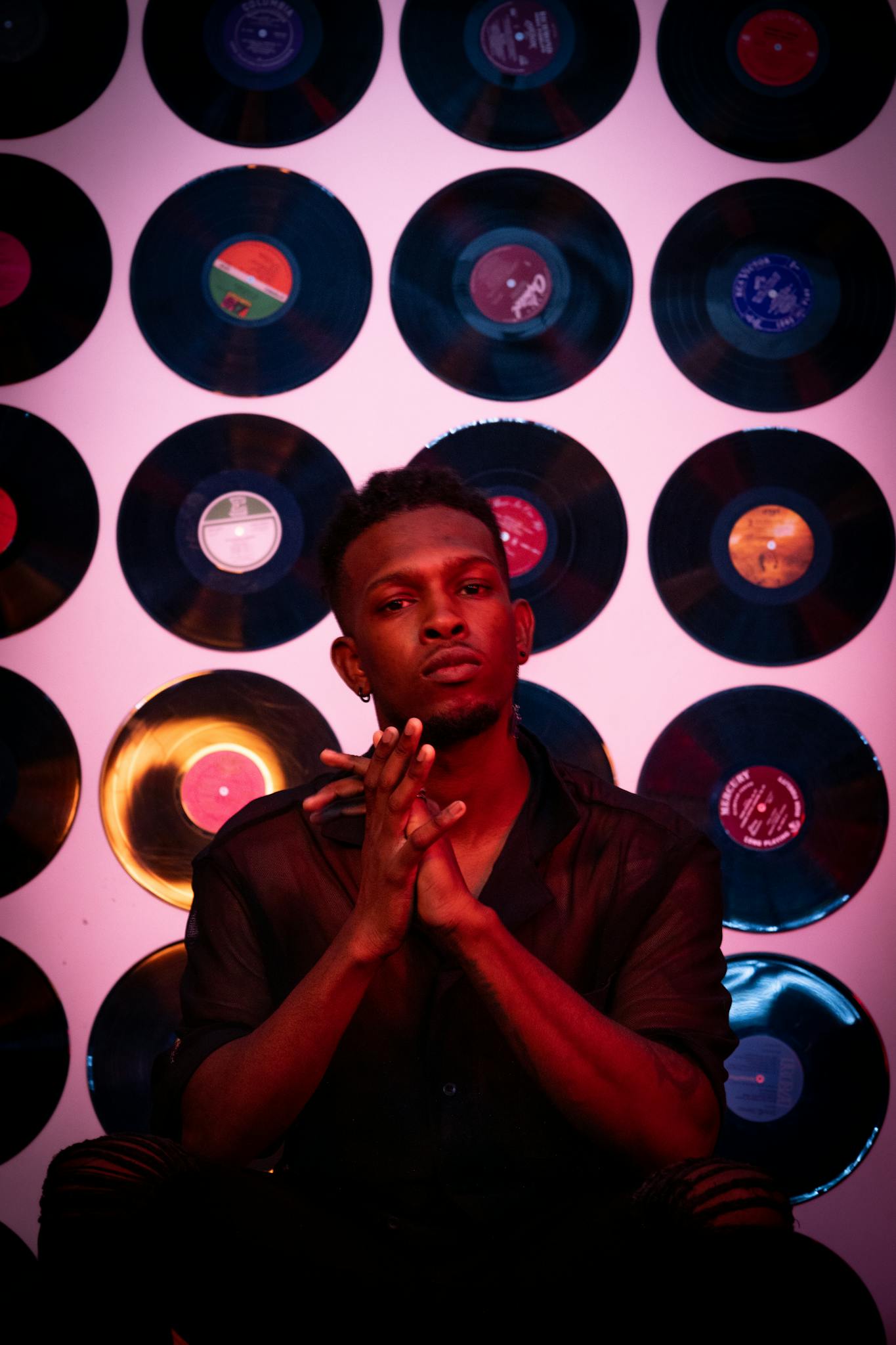 Artistic portrait of a man sitting in front of a vinyl records backdrop, featuring moody lighting.